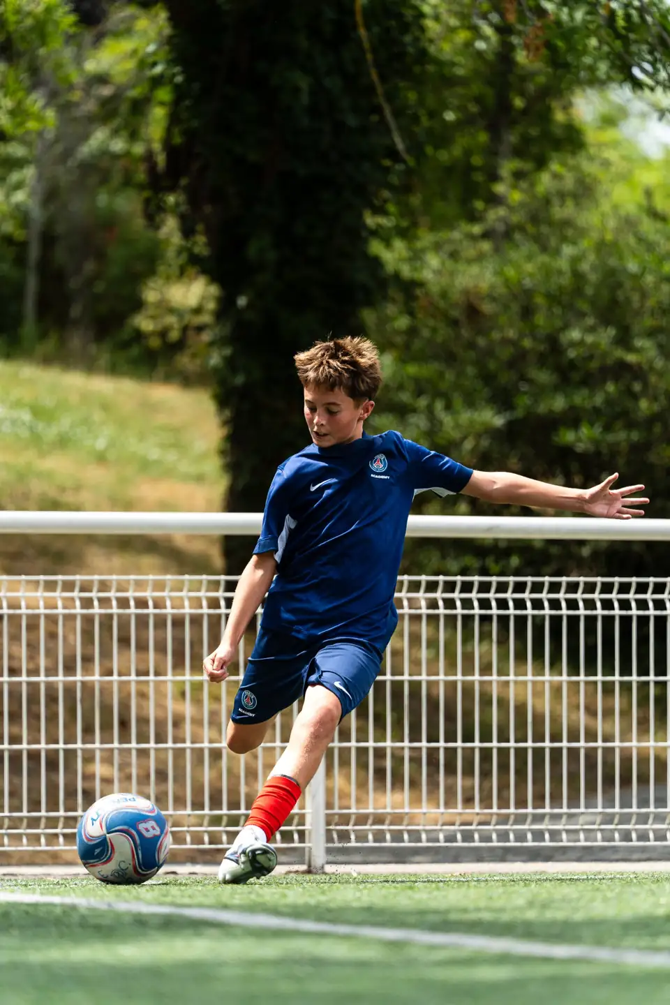 Jeune joueur frappant le ballon sur un terrain synthétique