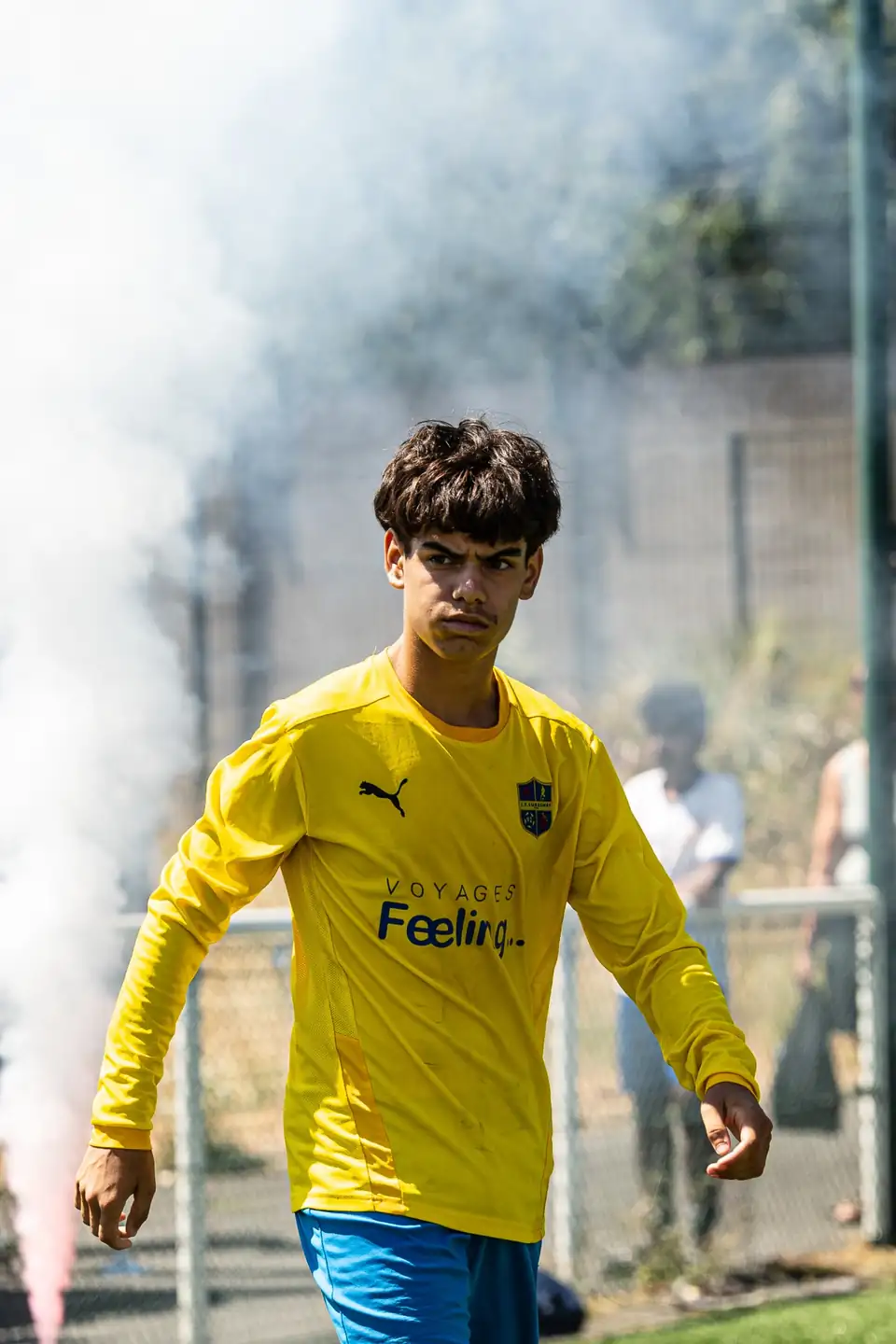 Jeune joueur en jaune entrant sur le terrain dans les fumigènes